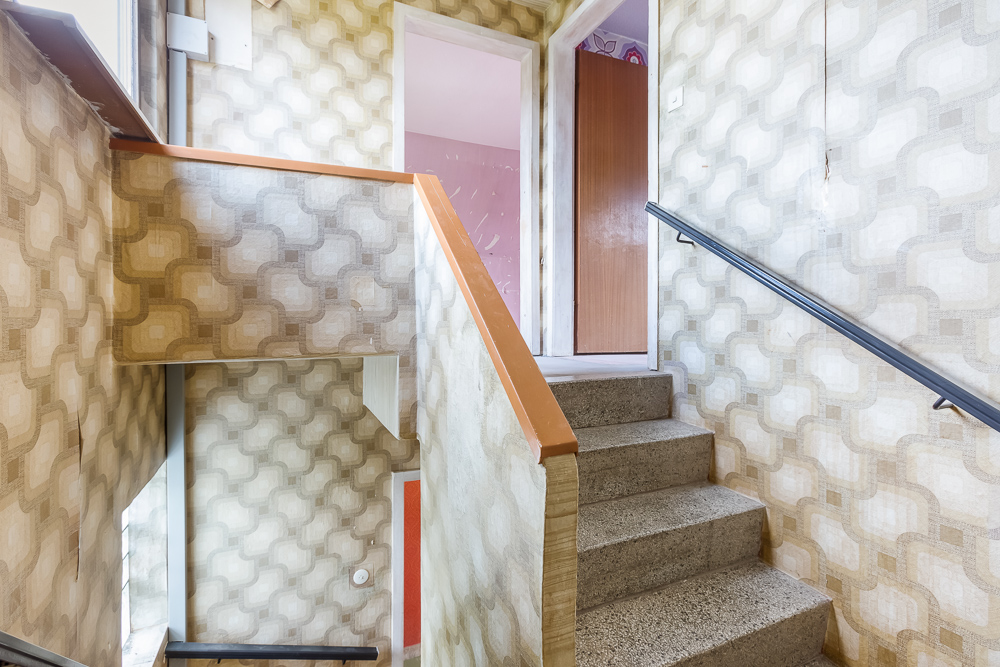 Treppe in einem Haus mit gemusterter Tapete und offen stehender Tür im Obergeschoss.
