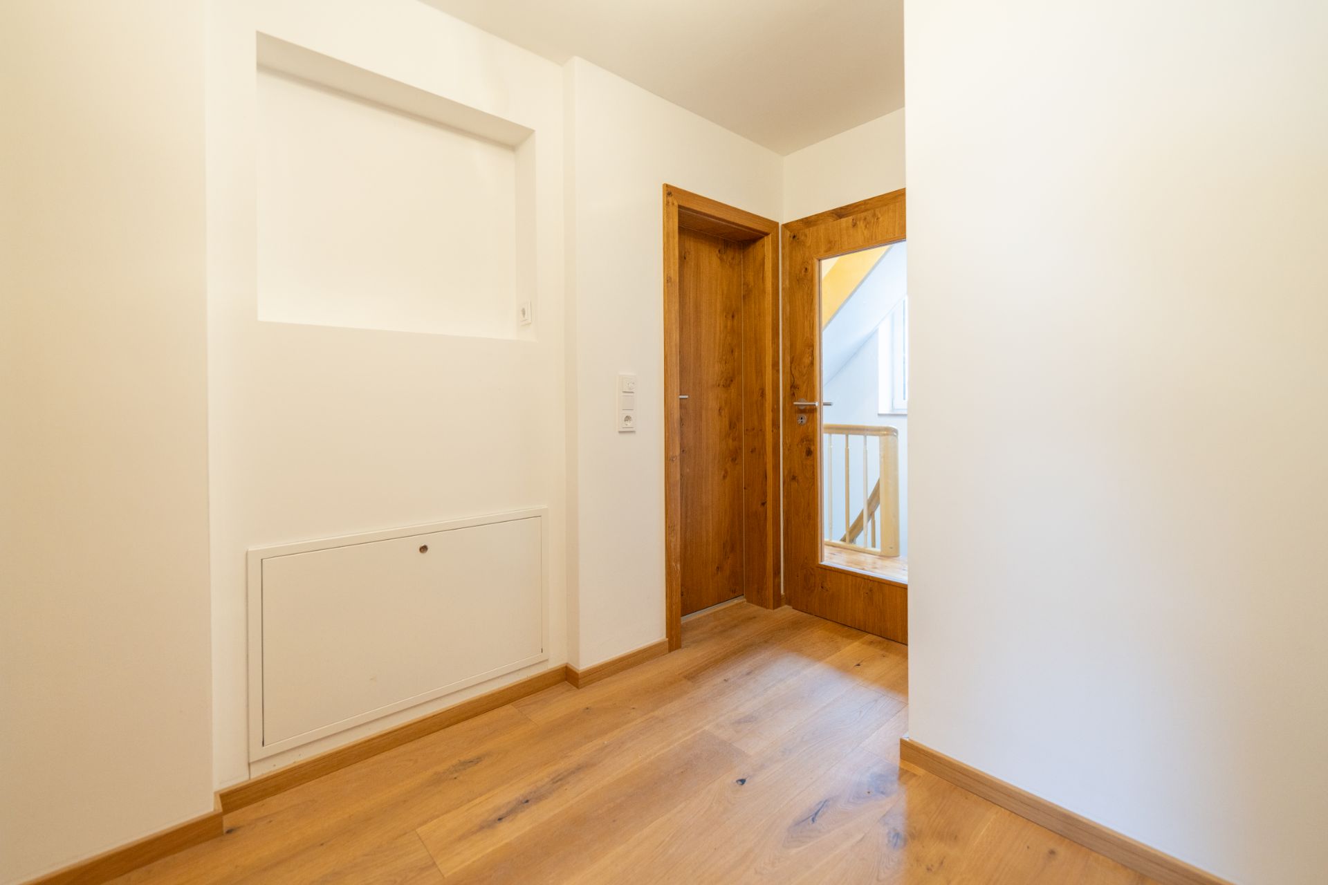 Heller Flur mit Holztür, Holzfußboden und weiß gestrichenen Wänden.