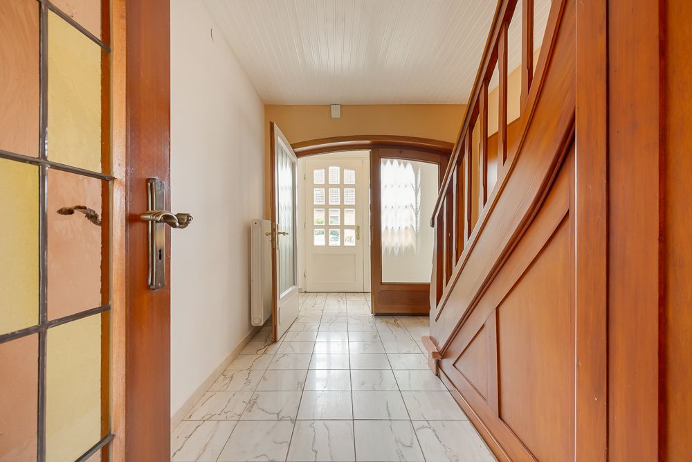 Heller Flur mit weißer Eingangstür, gefliestem Boden und Holztreppe.