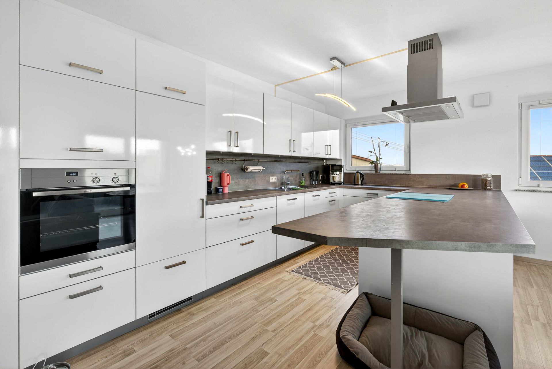Moderne Küche mit weißen Schränken, Elektrogeräten, Kochinsel und Hundebett auf Holzfußboden.