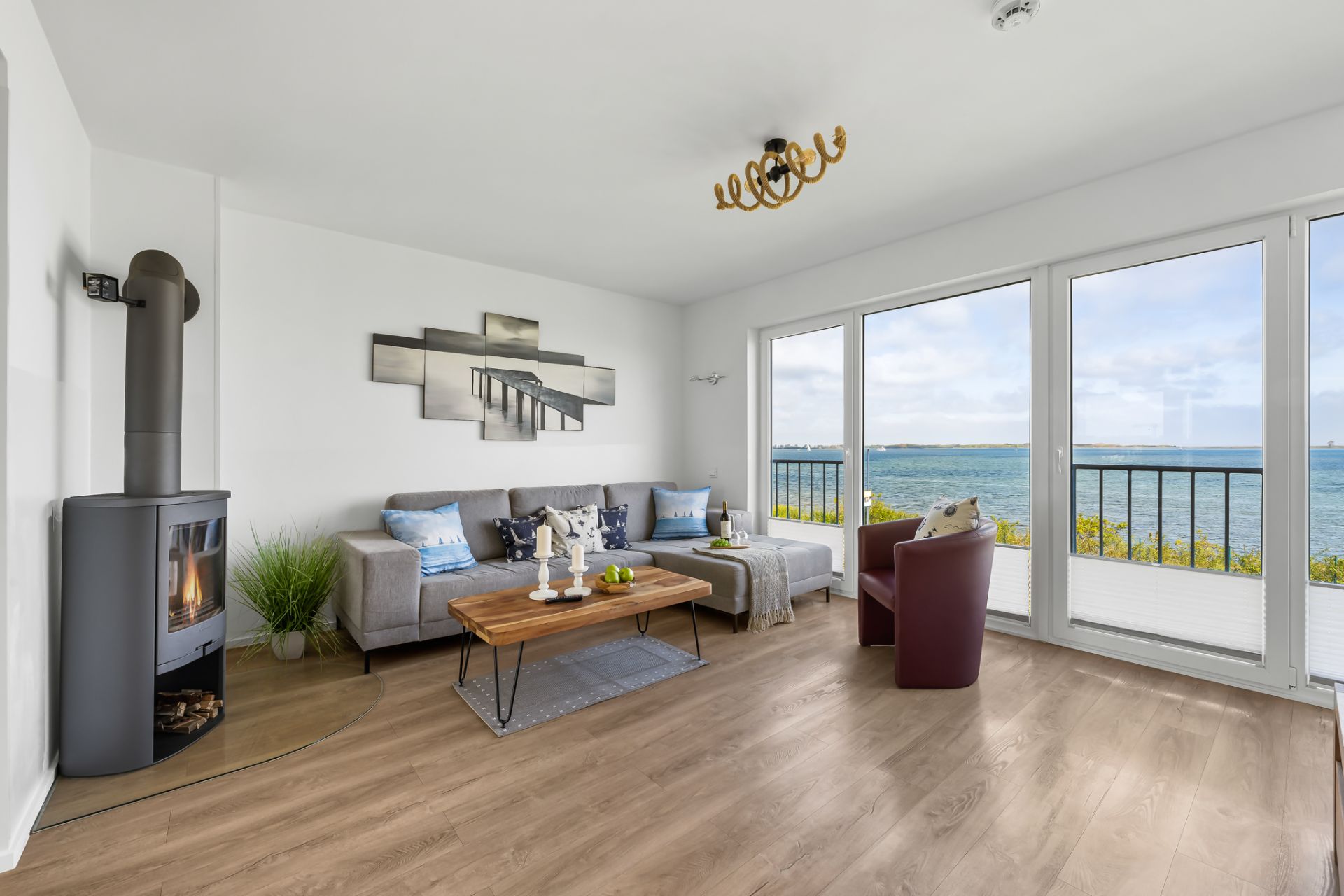 Helles Wohnzimmer mit Kamin, Sofa, Sessel und großen Fenstern mit Meerblick.