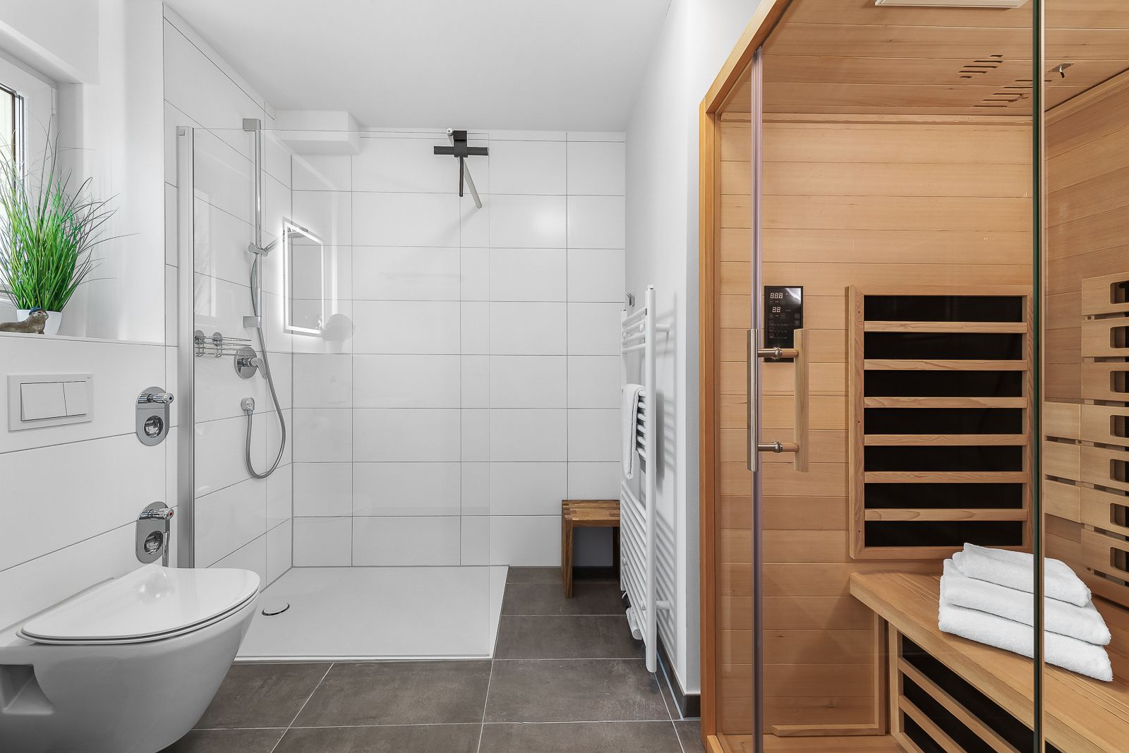 Modernes Badezimmer mit Dusche, Toilette, Handtuchwärmer und Holzsauna mit Handtüchern.