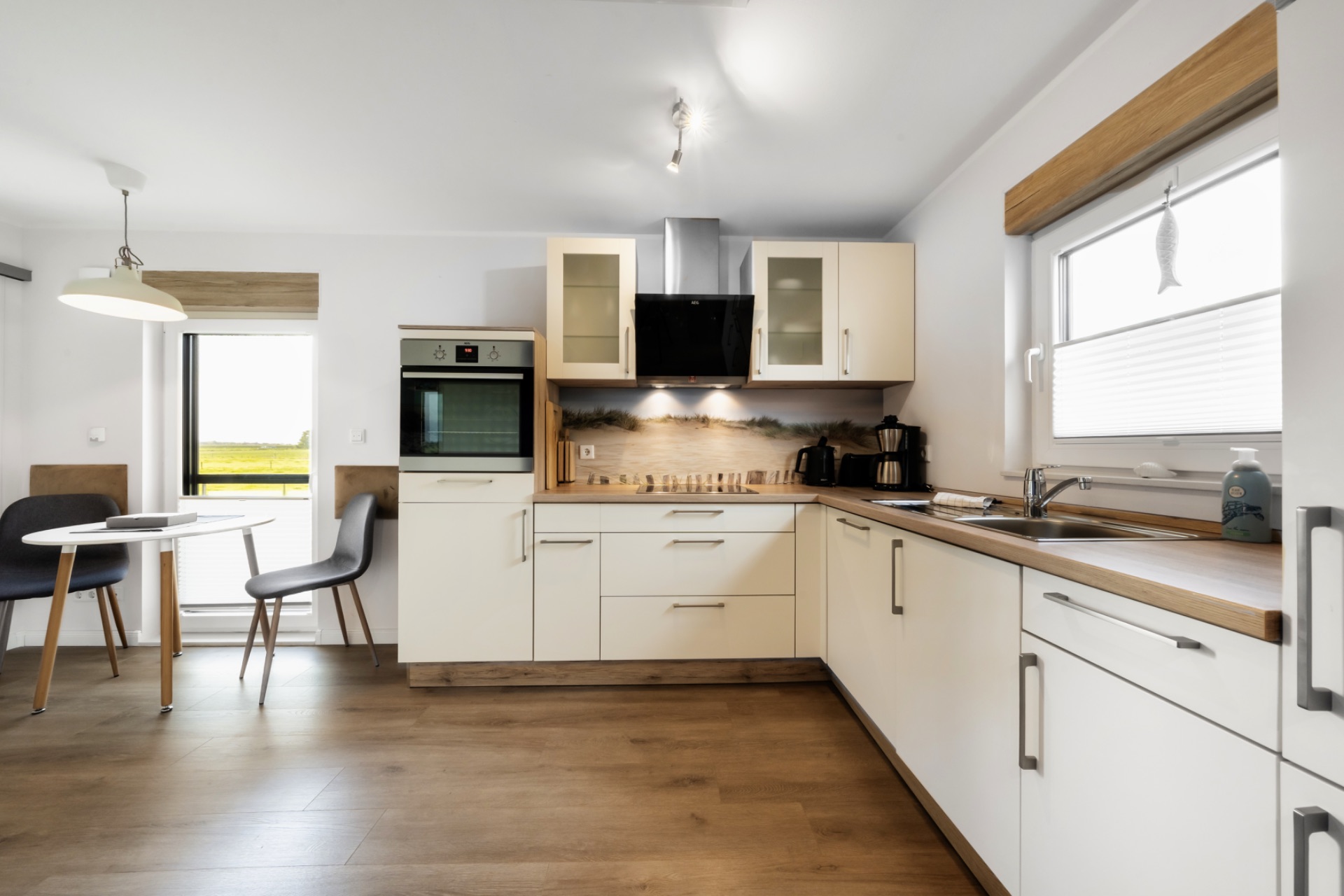 Moderne Küche mit weißen Schränken, Holzboden, Esstisch und zwei Stühlen am Fenster.
