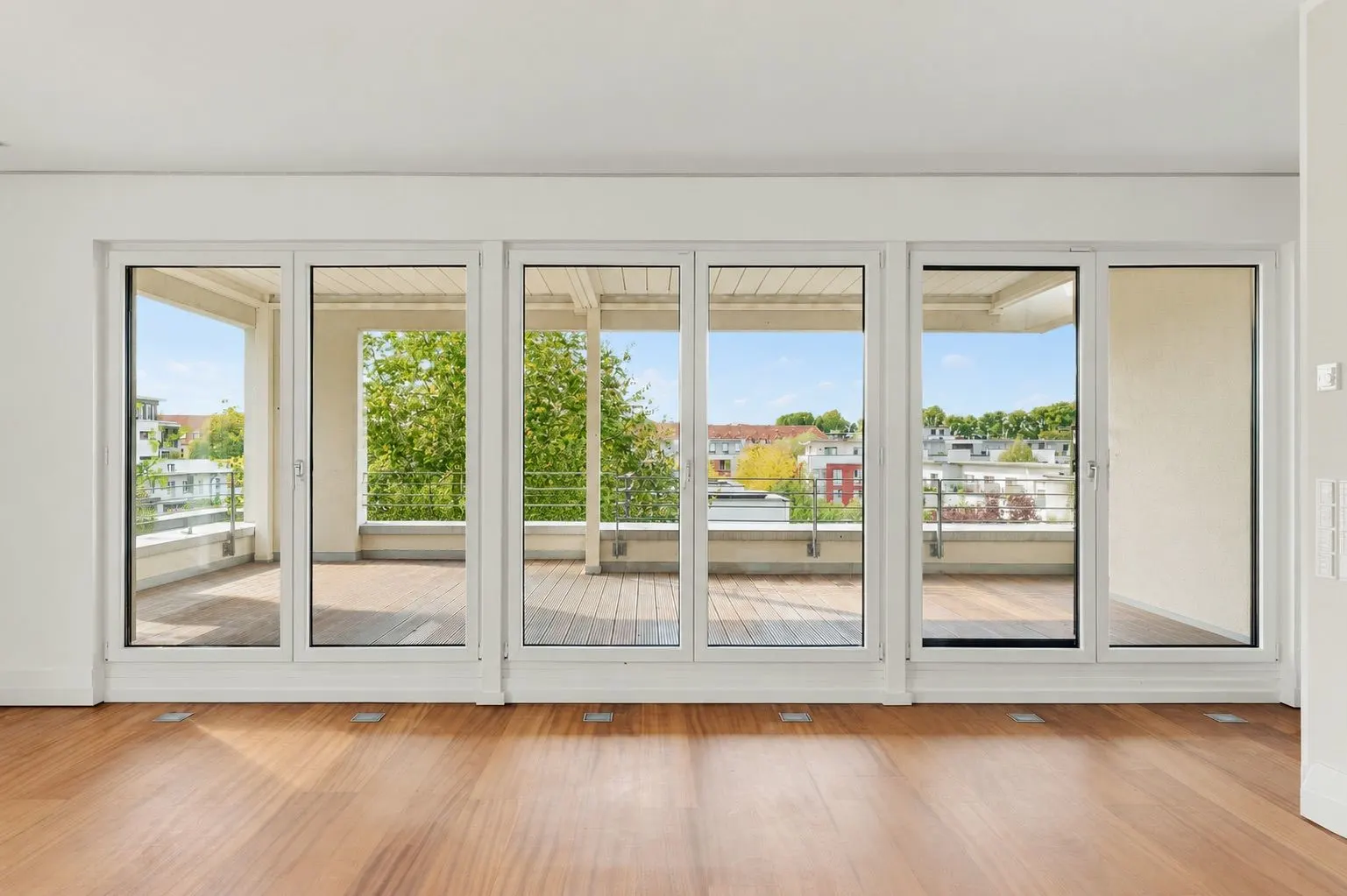 Helles Wohnzimmer mit großen Glas-Schiebetüren zu einem Balkon mit Blick ins Grüne.