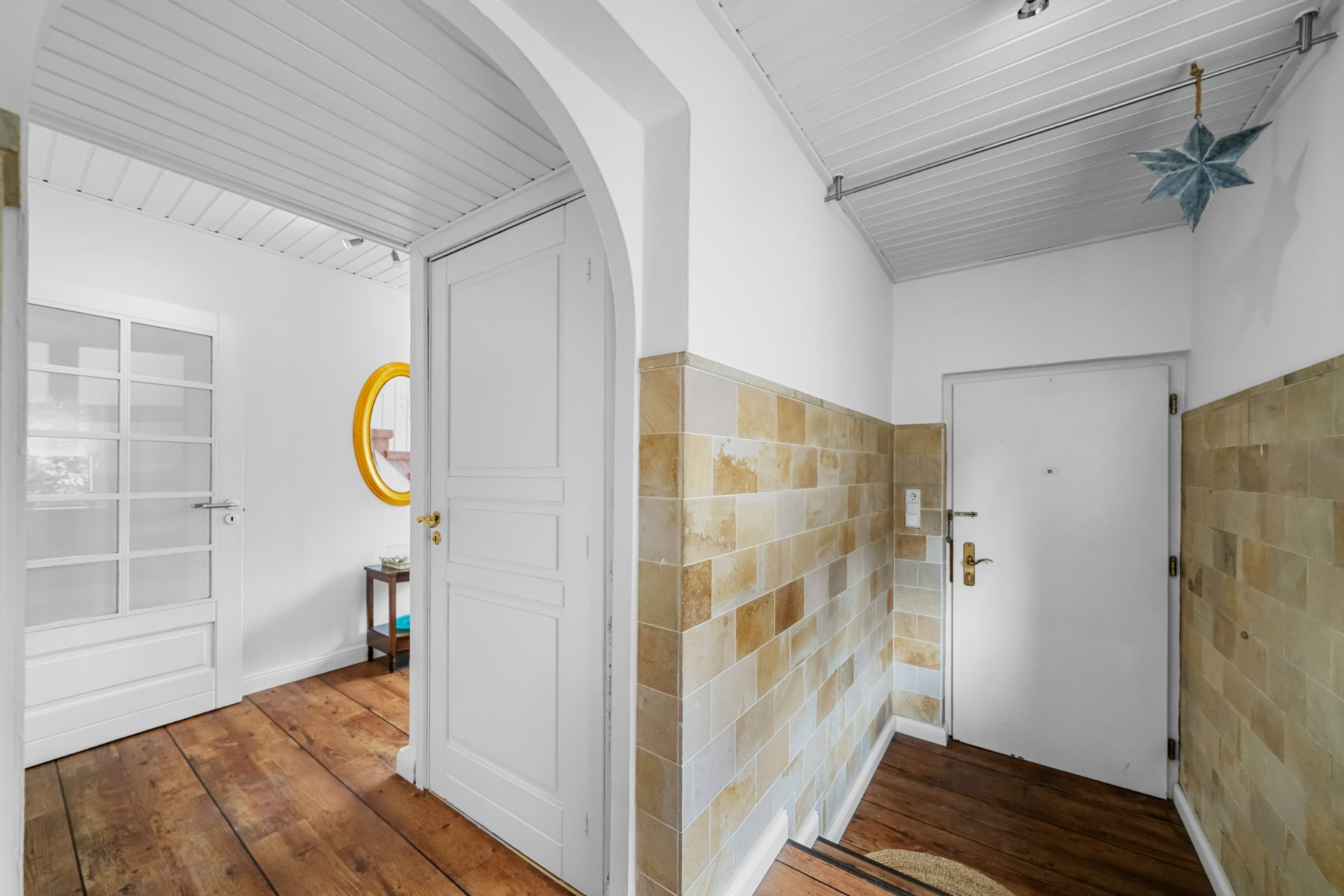 Heller Flur mit Holzboden, weißen Türen und beigen Wandfliesen.
