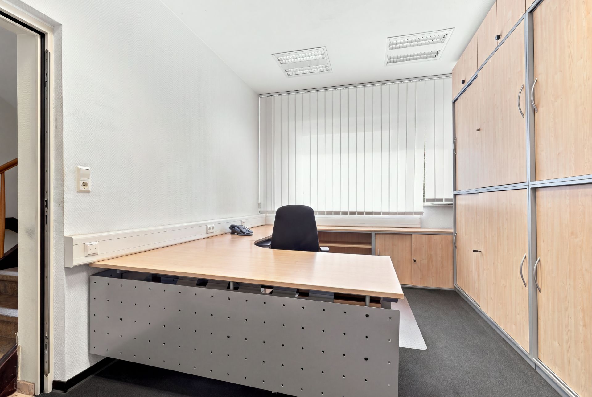 Büro mit großem Schreibtisch, Bürostuhl und mehreren Holzschränken an der Wand.