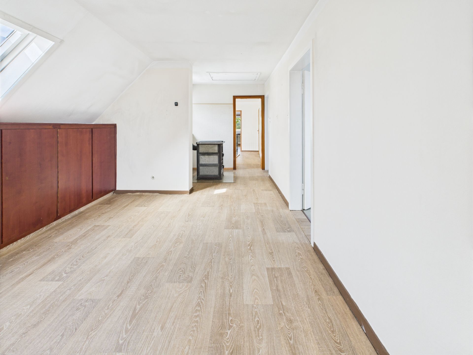Heller Raum mit Holzfußboden, weißen Wänden und Dachfenster, offene Tür im Hintergrund.