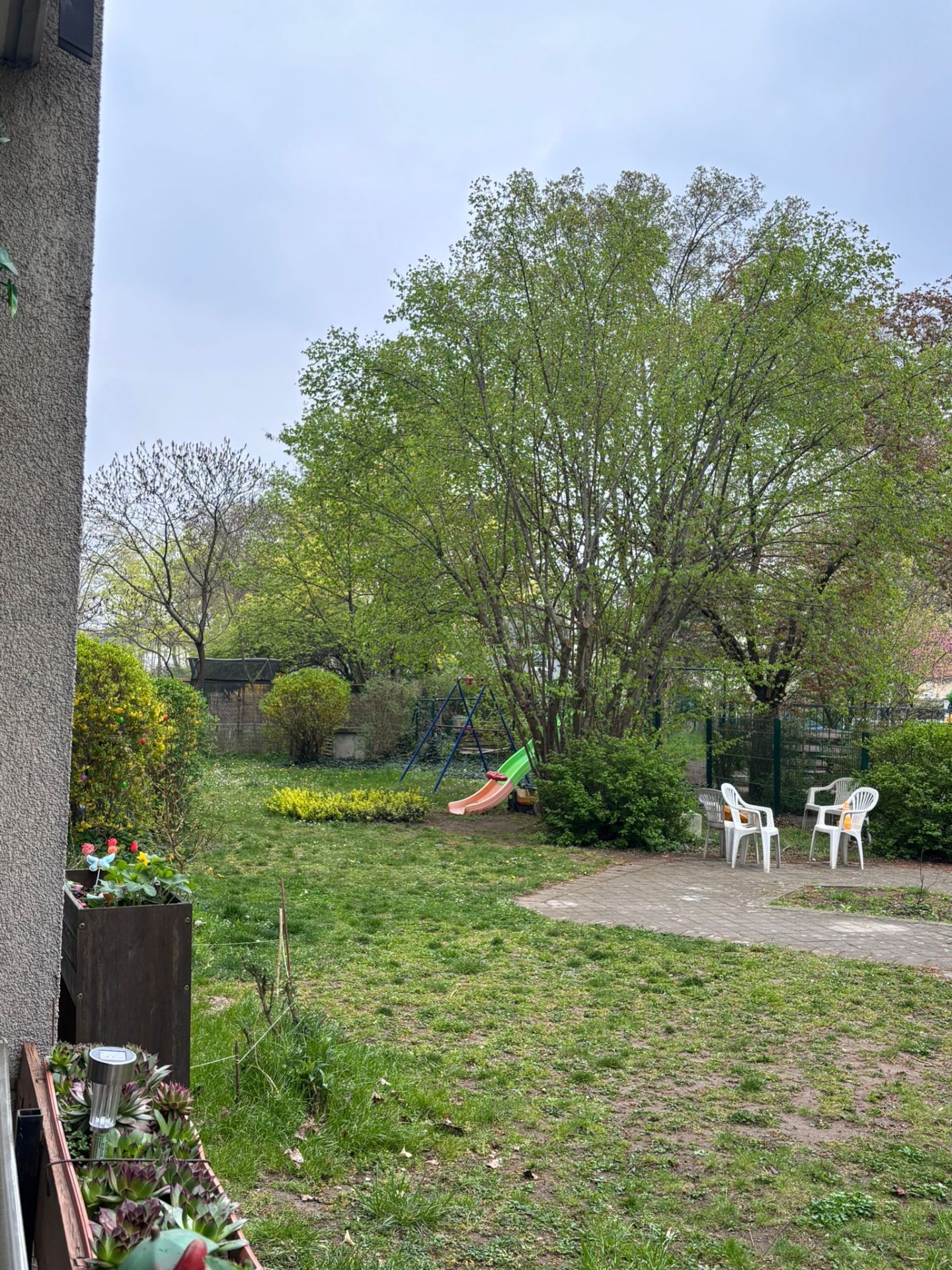 Garten mit Rutsche, weißen Stühlen und vielen grünen Bäumen im Hintergrund.
