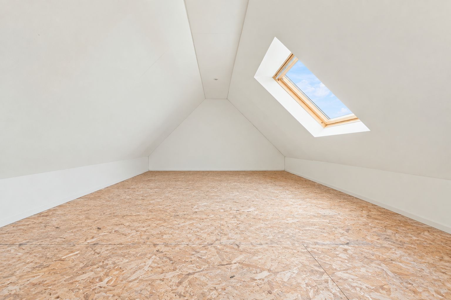 Leerer Dachbodenraum mit Holzfußboden und Dachfenster, durch das Tageslicht einfällt.