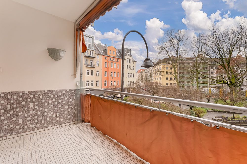Geräumiger Balkon mit Fliesenboden und Blick auf Wohnhäuser und Bäume.