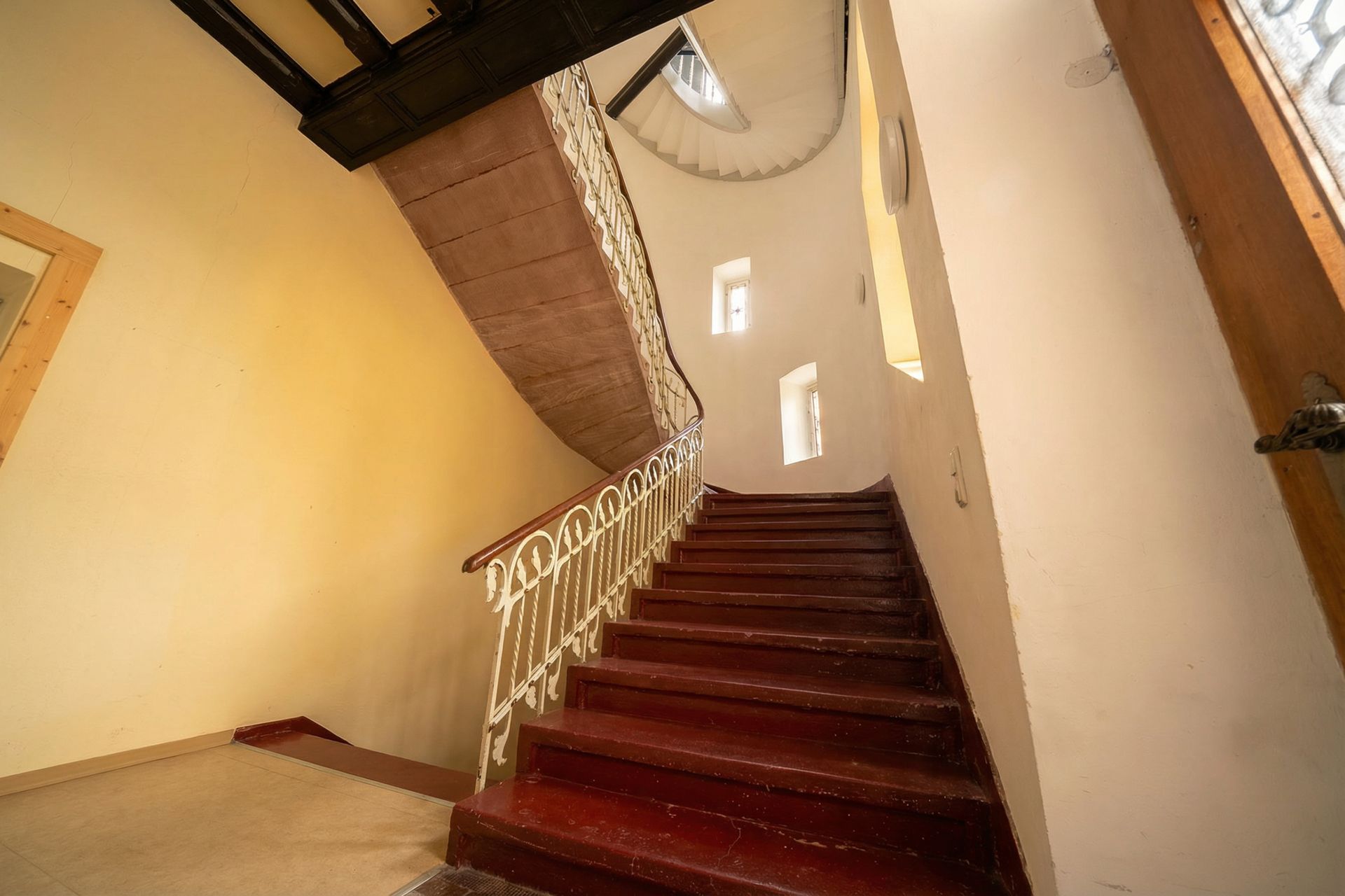 Treppe mit rotem Holz, weißem Geländer und cremefarbenen Wänden in einem Wohnhaus.