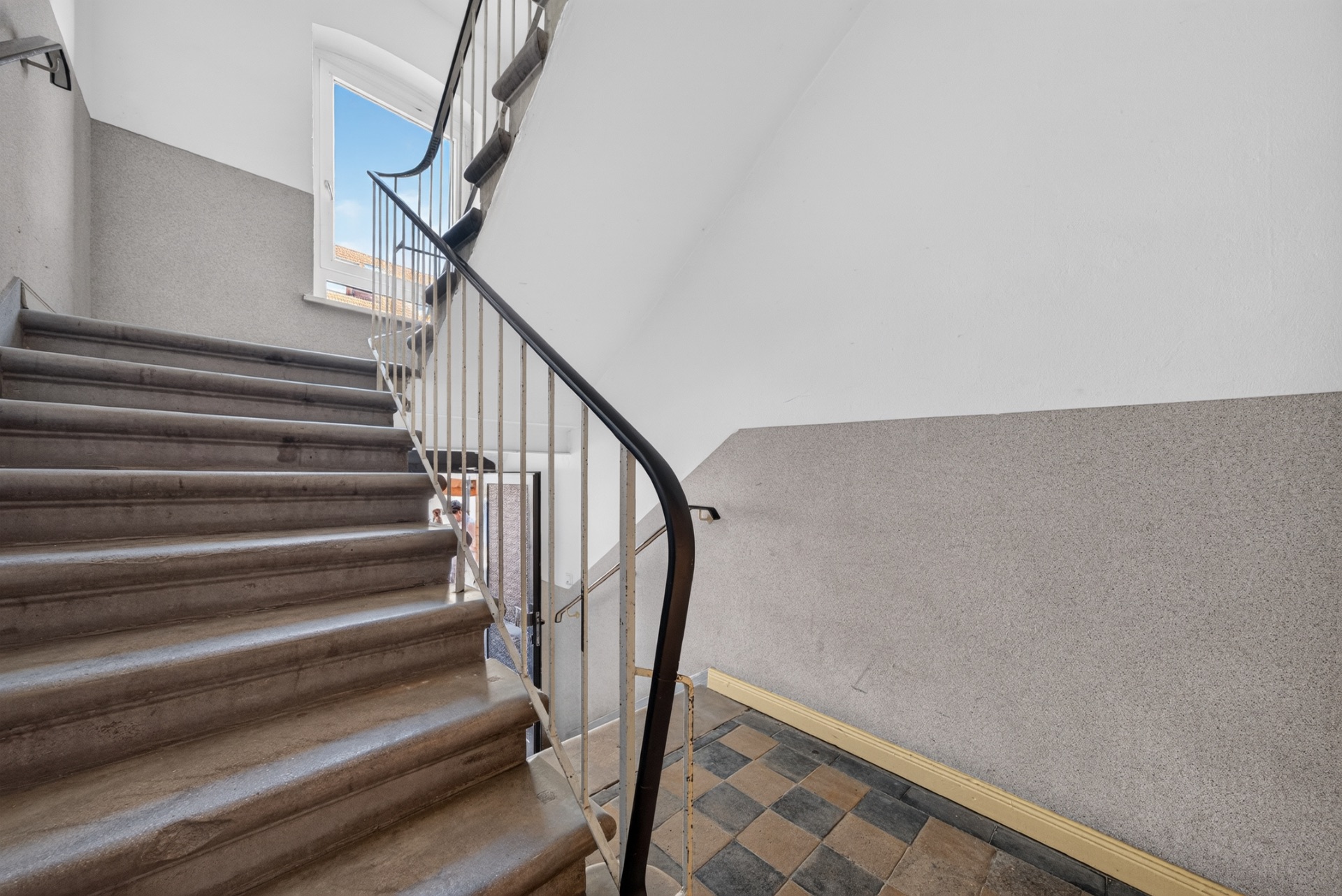 Treppenhaus mit brauner Treppe, Geländer und offenem Fenster am oberen Ende.