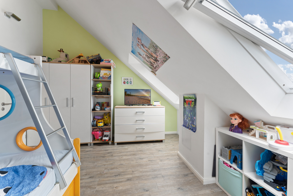 Helles Kinderzimmer mit Hochbett, Spielzeug, Regalen und einem großen Dachfenster.