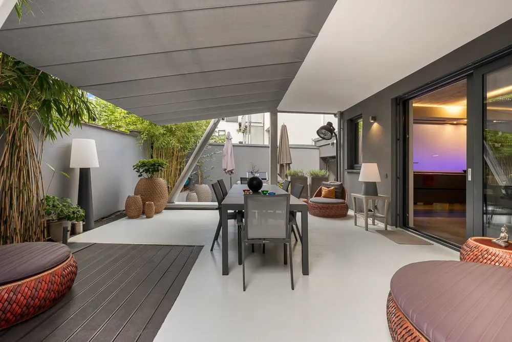 Überdachte Terrasse mit Esstisch, Sitzgelegenheiten, Pflanzen und modernen Lampen.