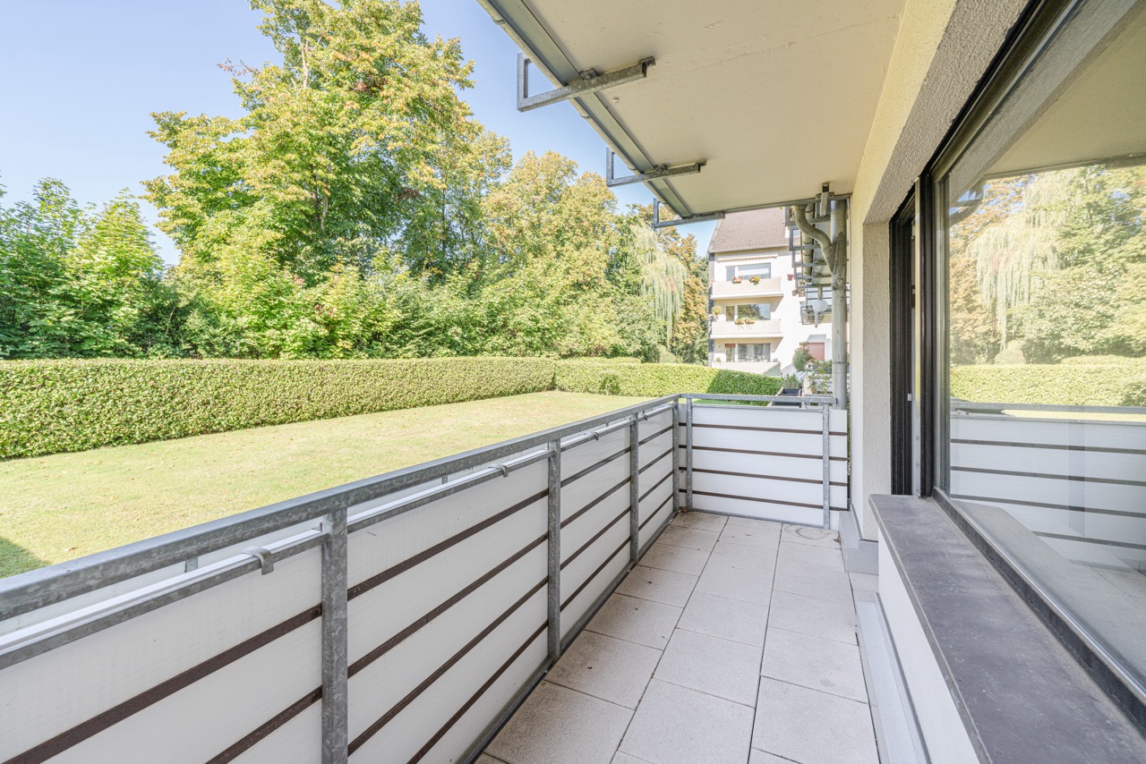 Balkon mit Metallgeländer und Blick auf einen grünen Garten mit Büschen und Bäumen.