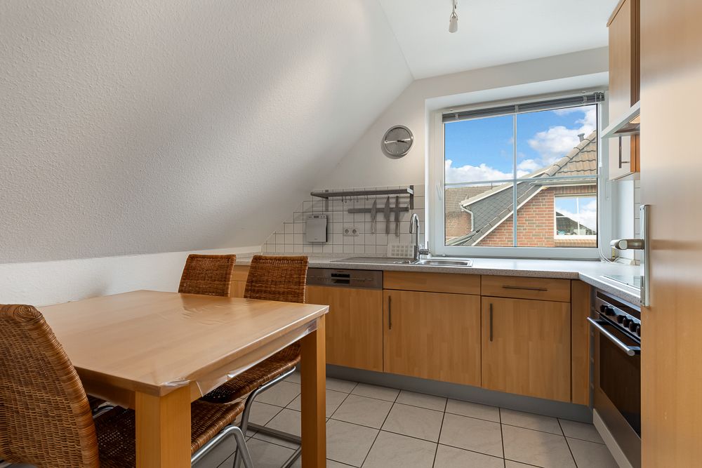 Moderne Küche mit Holzmöbeln, Esstisch und großem Fenster mit Blick auf Nachbarhäuser.