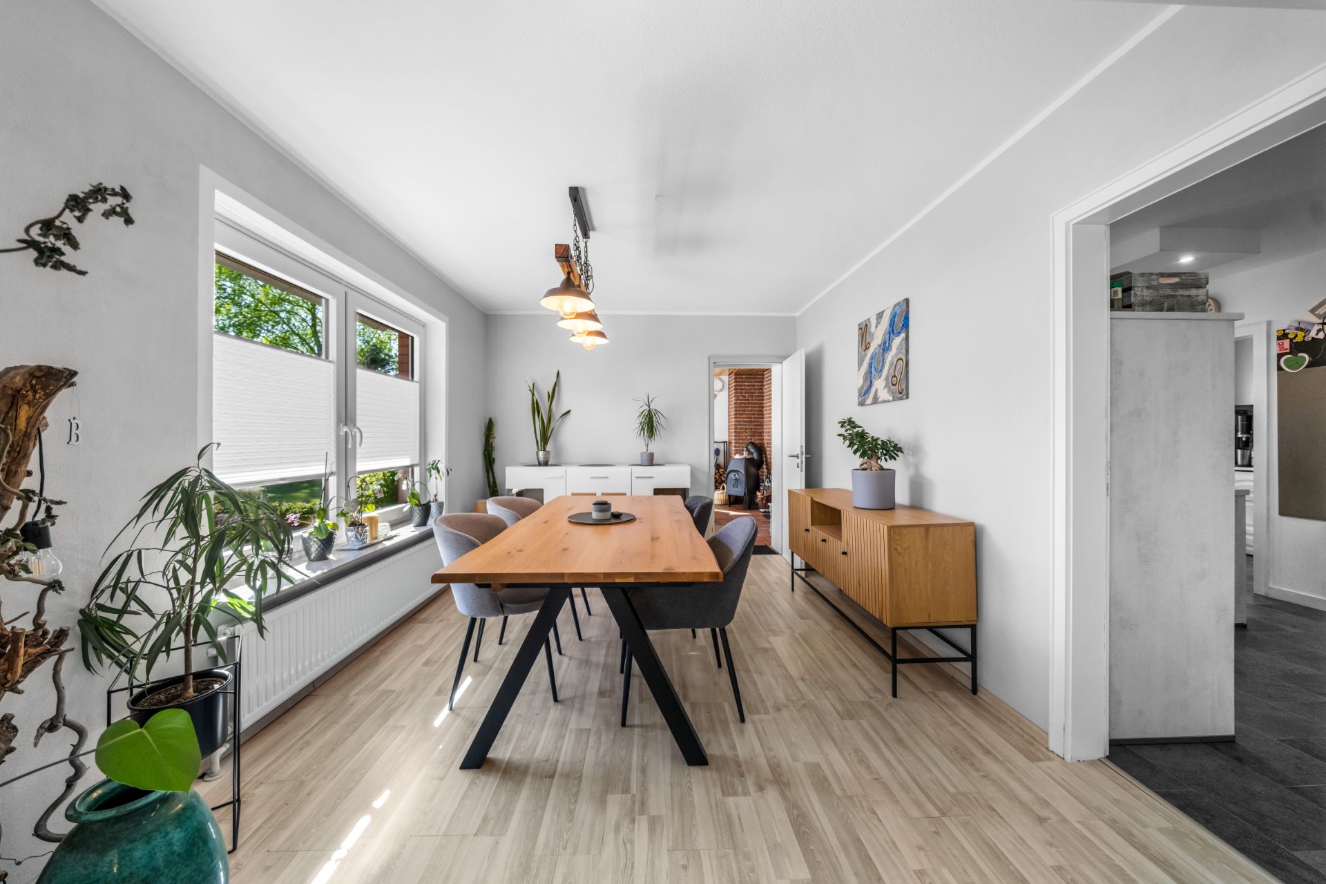 Heller Essbereich mit Holztisch, sechs Stühlen, Sideboards und Pflanzen am Fenster.