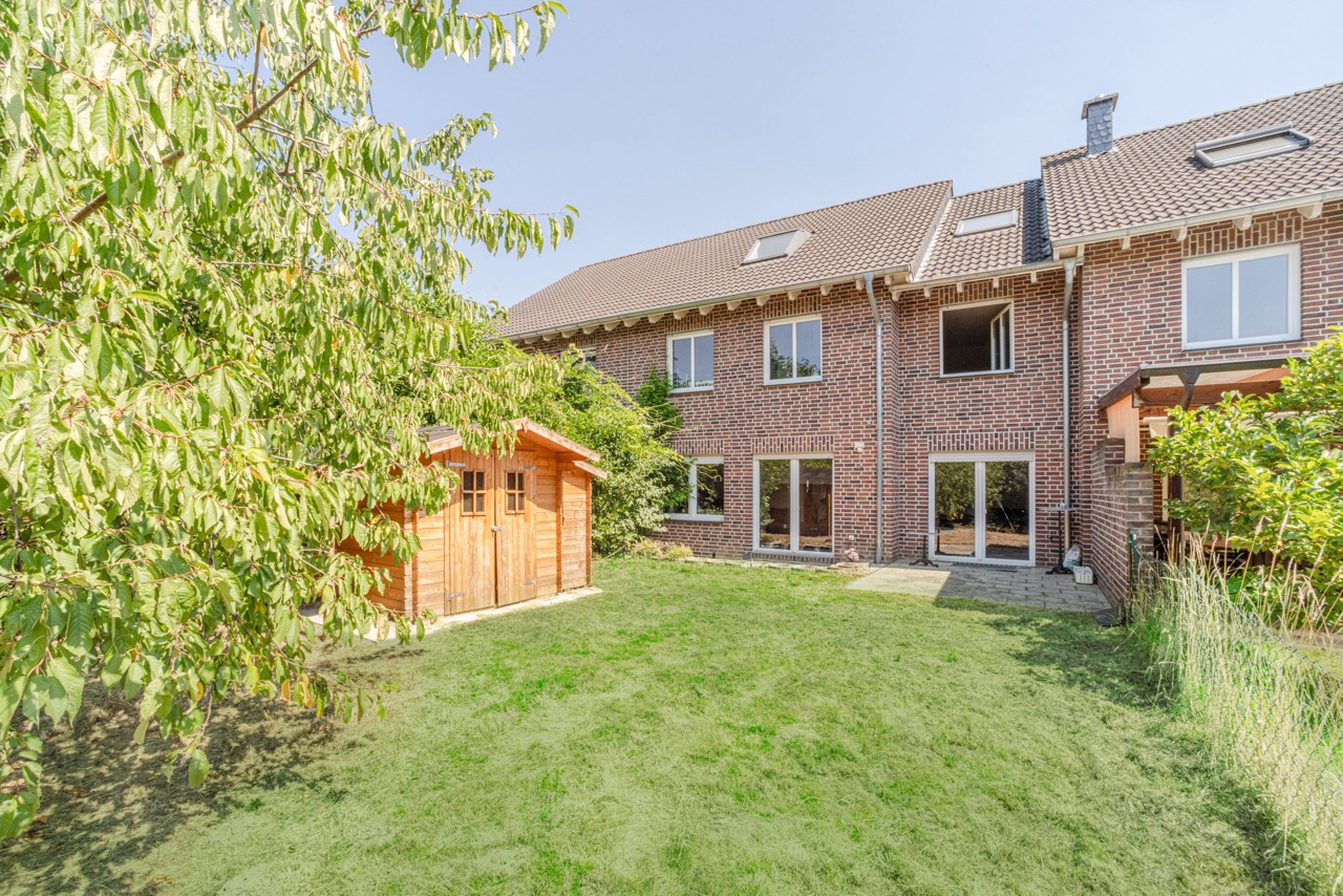 Garten mit Rasen, Holzhaus und Blick auf ein Backsteinwohnhaus mit vielen Fenstern.