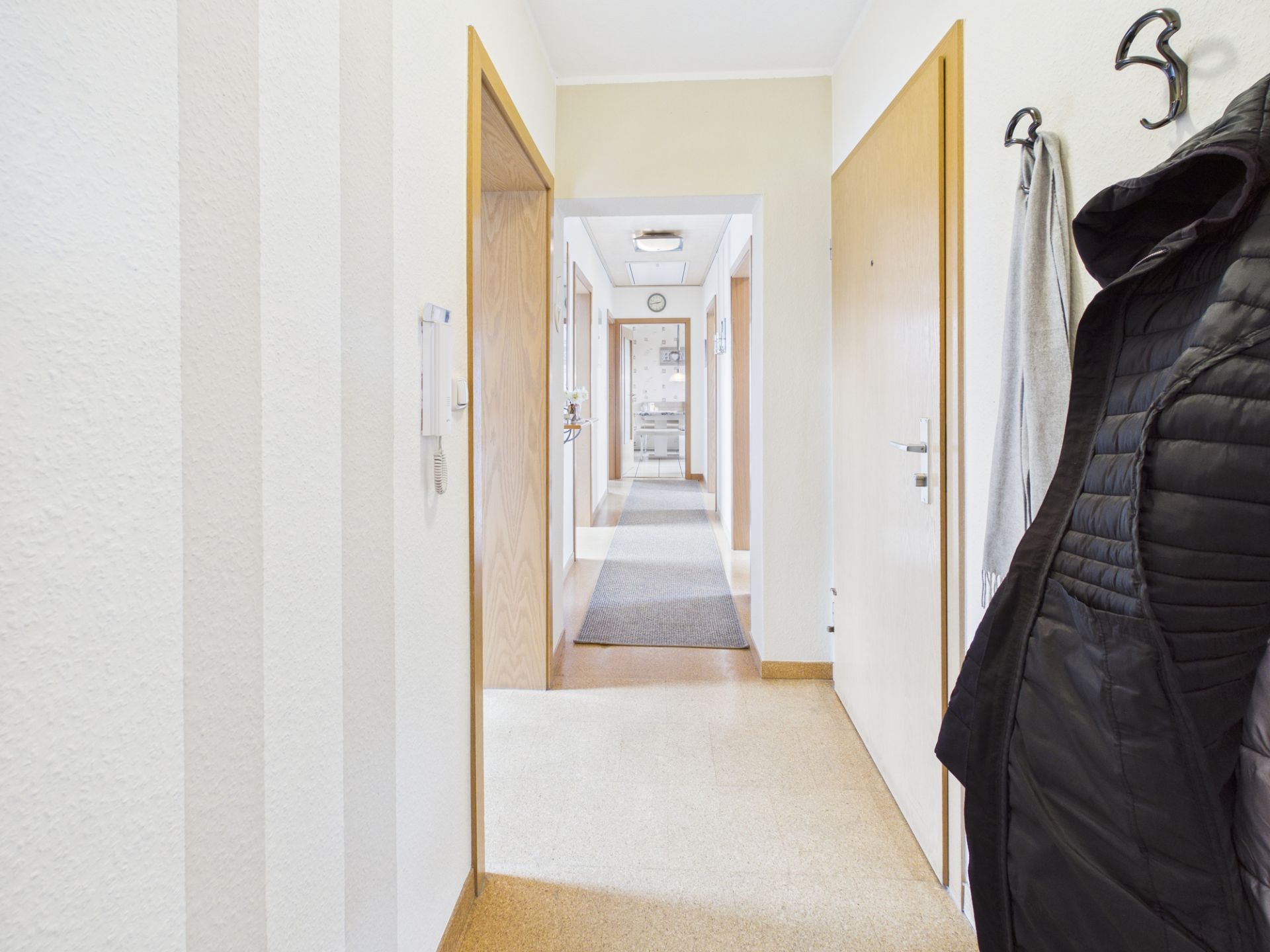 Heller Flur mit mehreren Türen, Jacke und Handtuch an Wandhaken, Teppichläufer am Boden.
