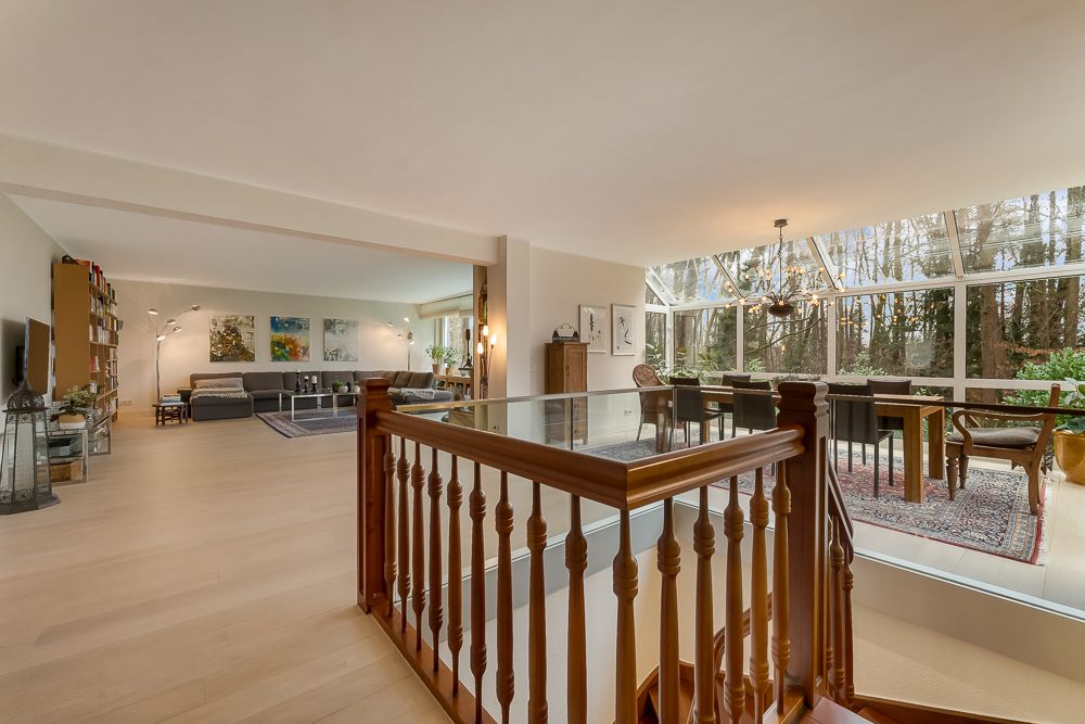 Großes Wohnzimmer mit Holzboden, Sitzecke und Essbereich mit Panoramafenstern zum Garten.