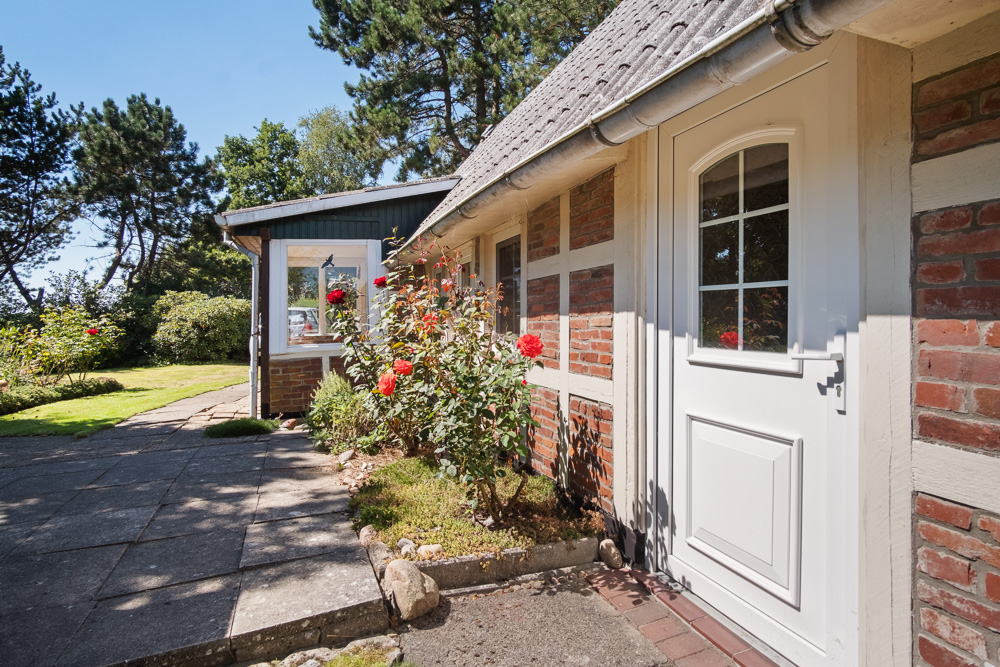 Eingangsbereich eines Hauses mit weißer Tür, Blumenbeet und rotem Backstein.