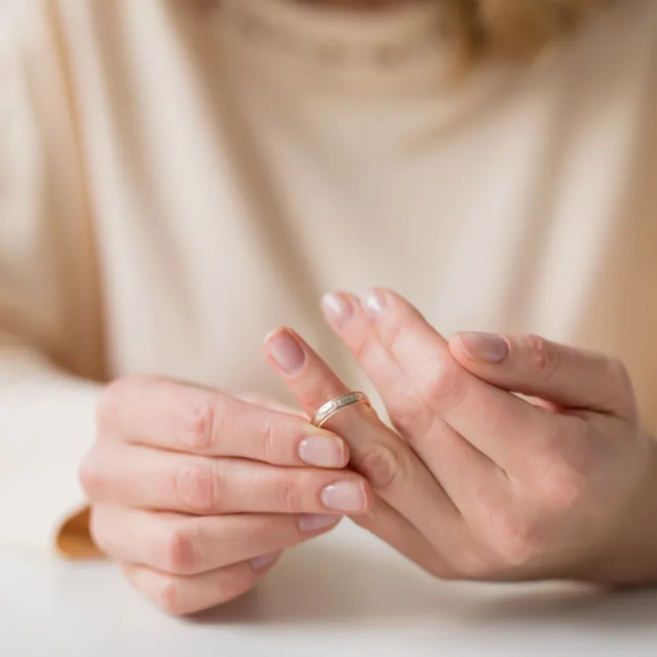 Nahaufnahme von Händen, die einen Ring vom Finger abziehen.