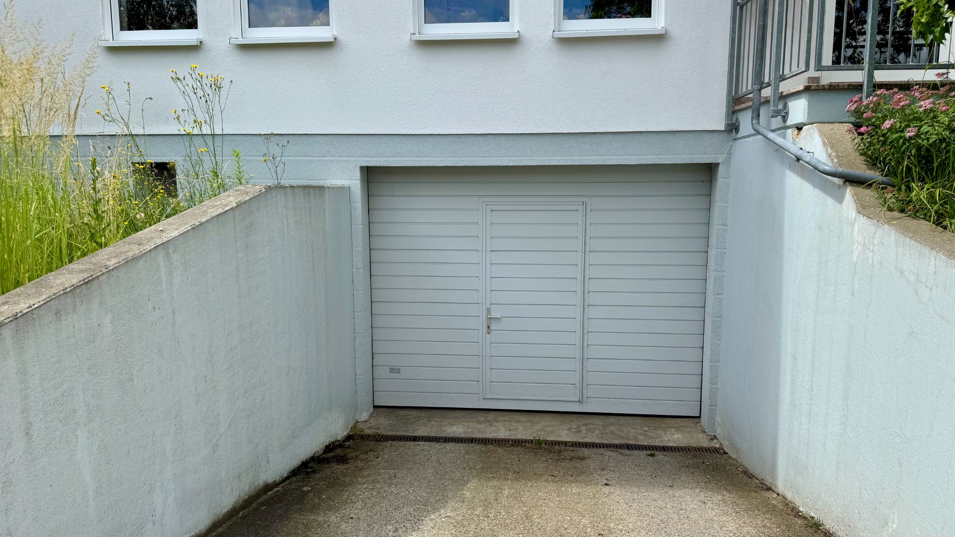 Abgesenkte Garageneinfahrt mit weißem Garagentor und drei Fenstern darüber.