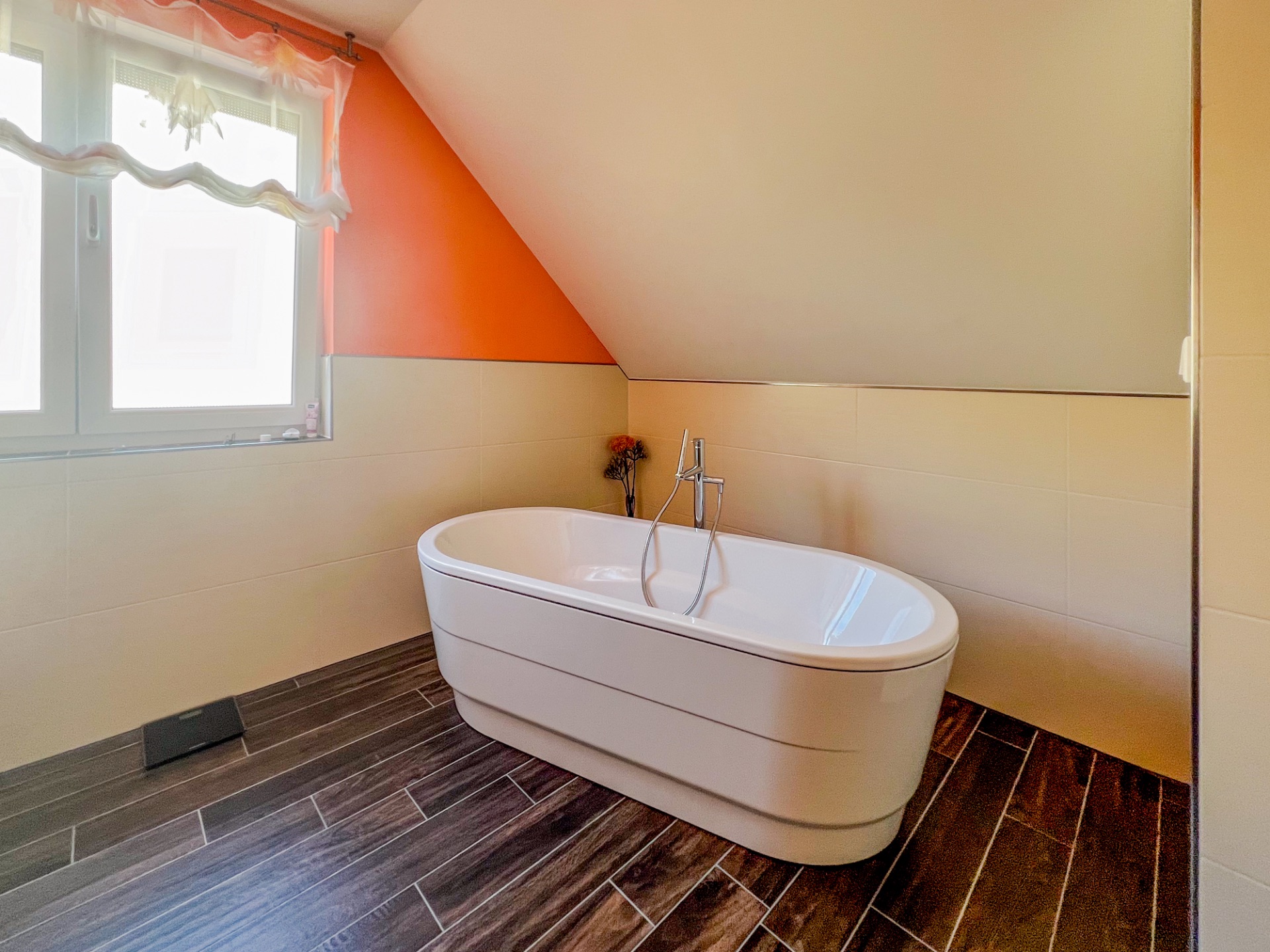 Modernes Badezimmer mit freistehender Badewanne unter einer Dachschräge und braunem Fliesenboden.