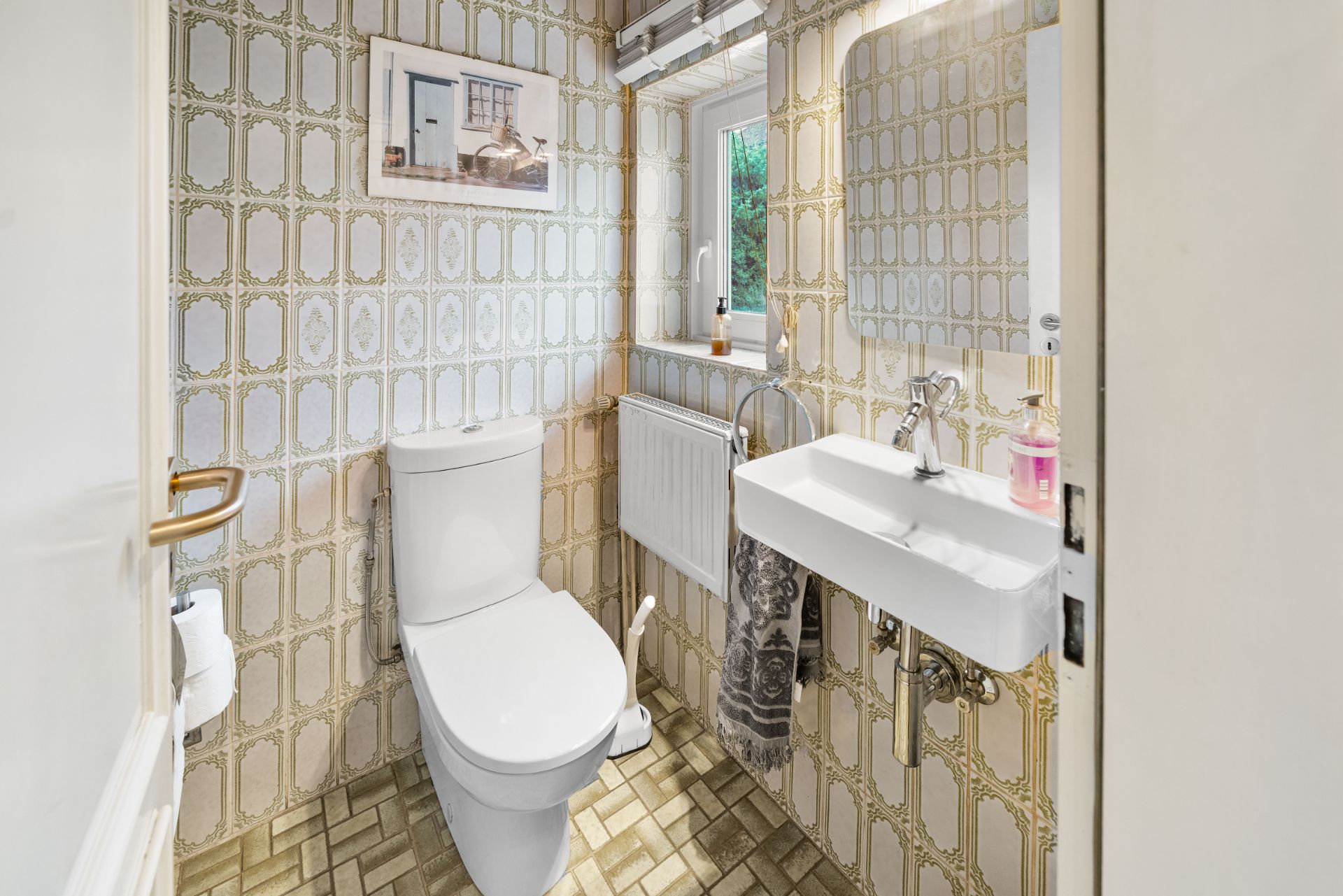 Kleines Badezimmer mit Toilette, Waschbecken, Spiegel und Fenster.