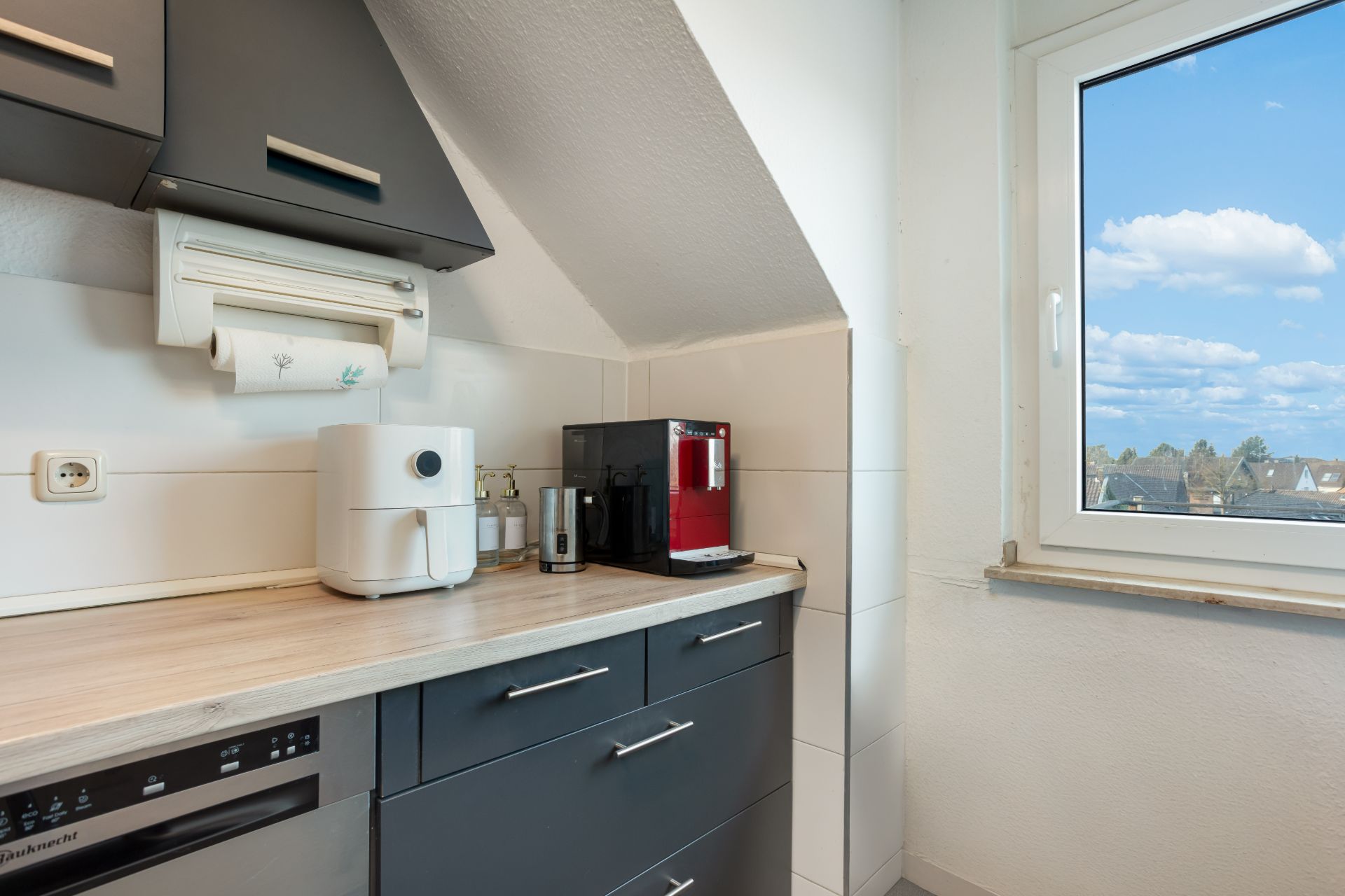 Moderne Küchenecke mit Kaffeemaschine, Heißluftfritteuse, Fenster und Ober- sowie Unterschränken.