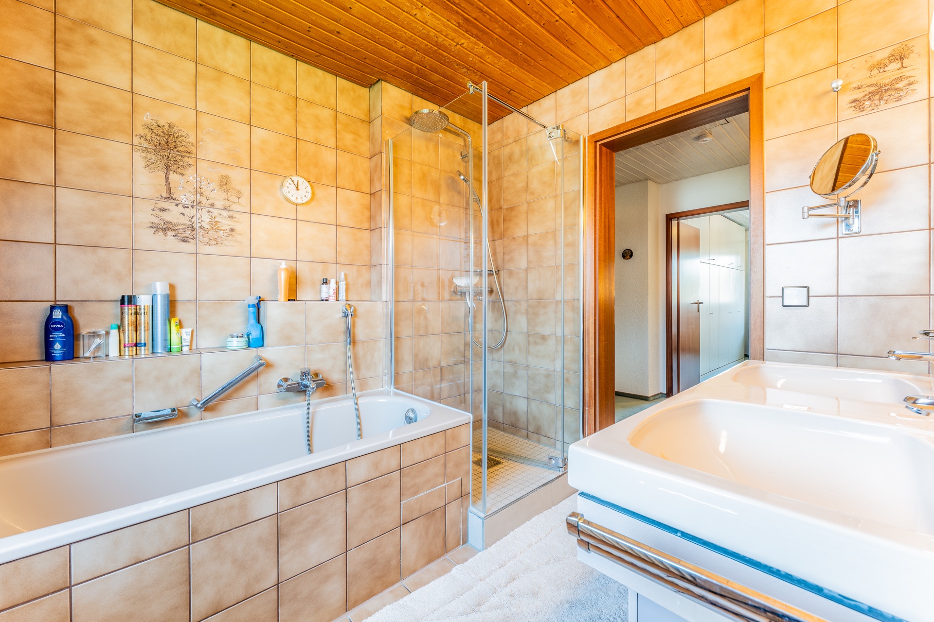 Helles Badezimmer mit Badewanne, Dusche, Doppelwaschbecken und beigefarbenen Fliesen.