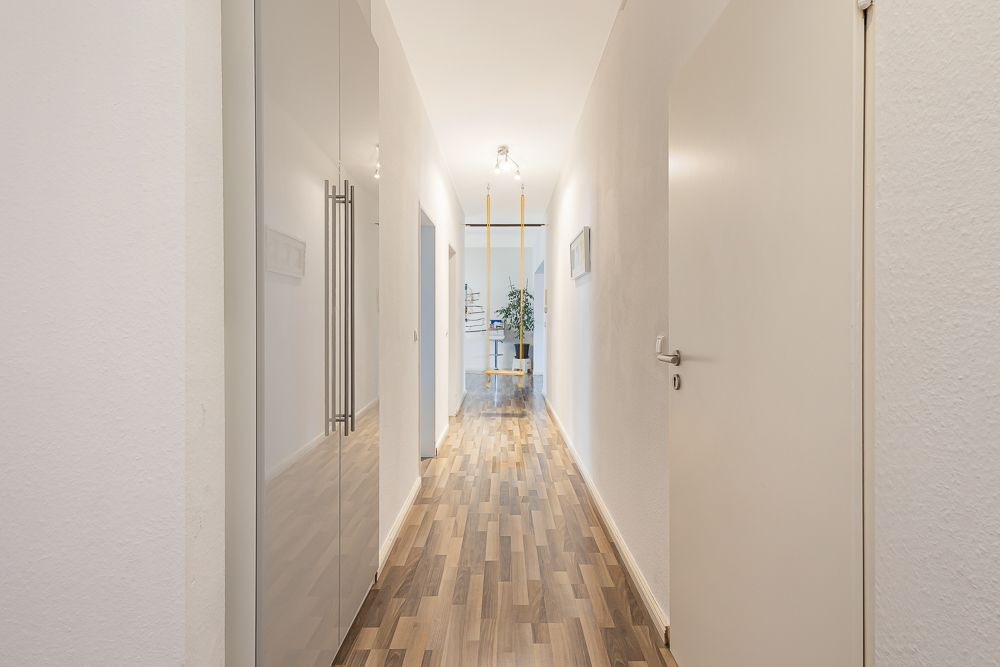 Heller Flur mit Holzboden, weißen Türen und einem Schrank an der linken Wand.