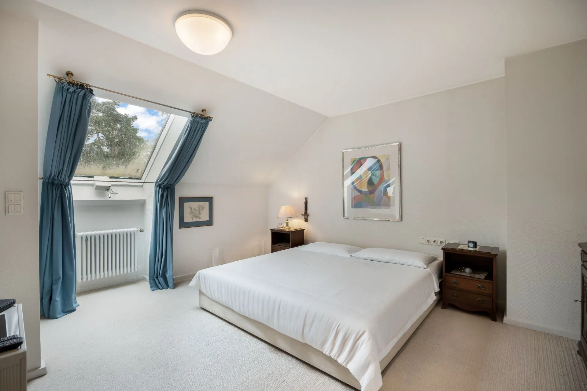 Helles Schlafzimmer mit Doppelbett, blauen Vorhängen und Dachfenster.