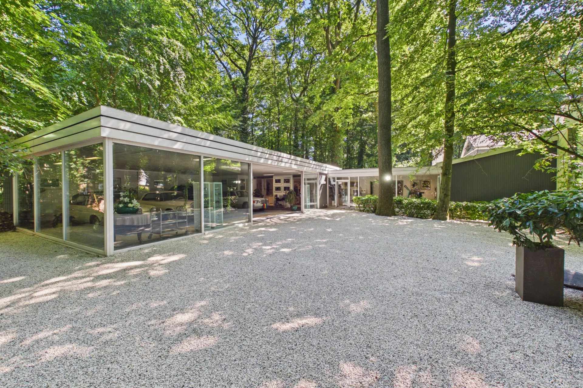 Modernes Wohnhaus mit großen Glasfronten, umgeben von Bäumen und Kiesfläche im Vordergrund.