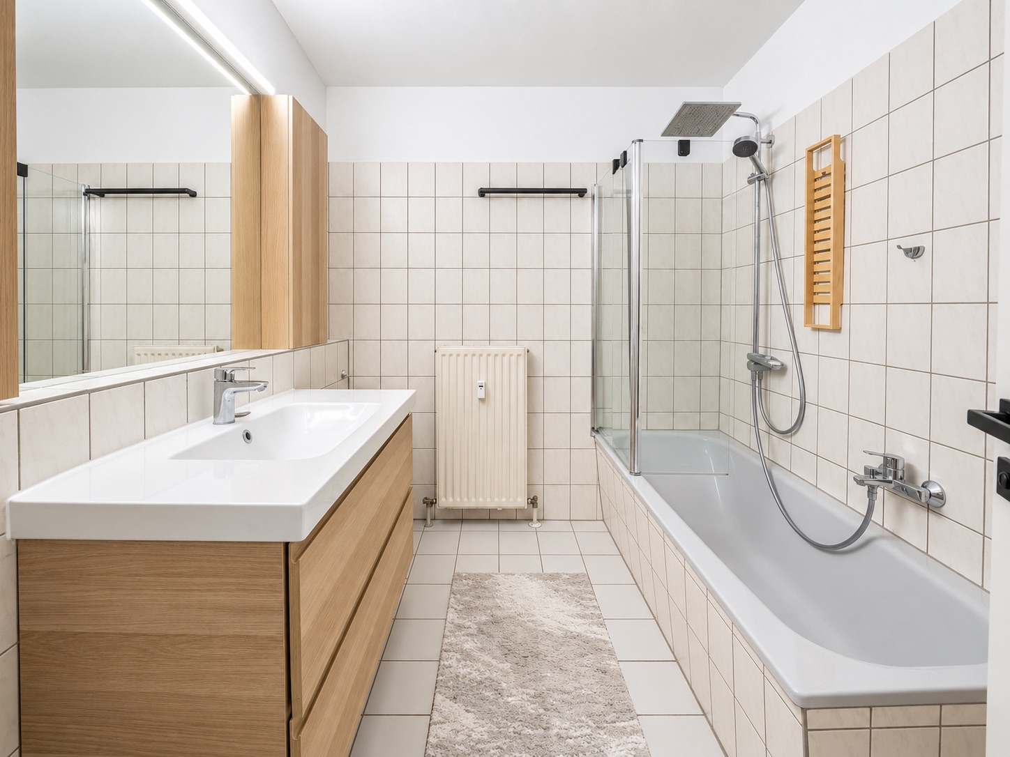 Modernes Badezimmer mit Badewanne, Waschbecken, Spiegel und hellen Fliesen.