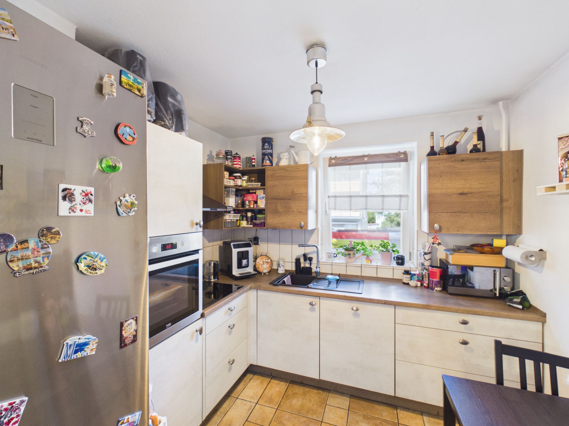 Helle Küche mit Eckspüle, Kühlschrank mit Magneten und zwei Fenstern.