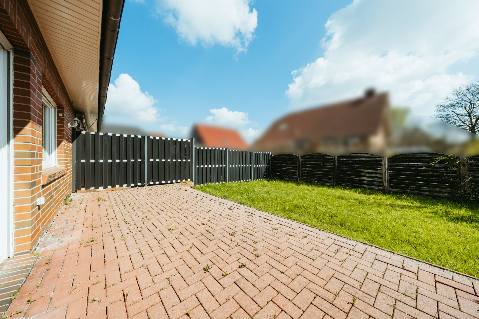Gepflasterte Terrasse mit angrenzender Rasenfläche und Holzzaun im Garten.
