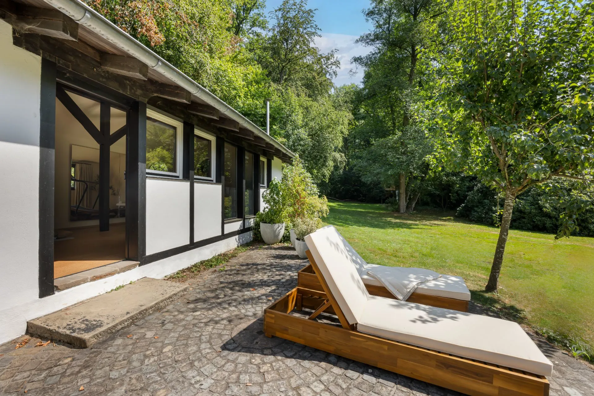 Zwei Liegestühle auf einer Steinterrasse vor einem Haus mit Blick auf einen grünen Garten.