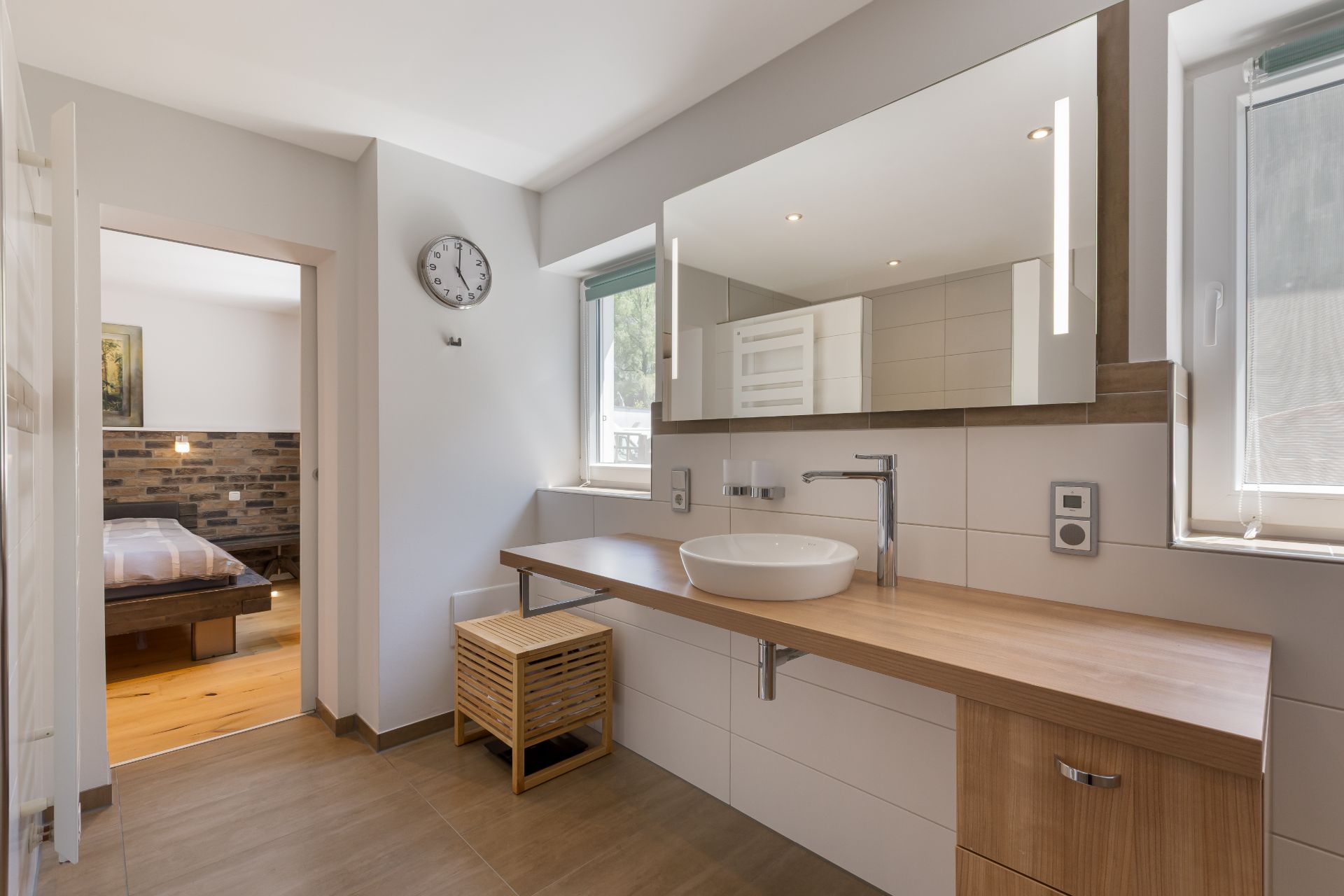 Modernes Badezimmer mit Holzwaschtisch, großem Spiegel und Blick in ein Schlafzimmer.