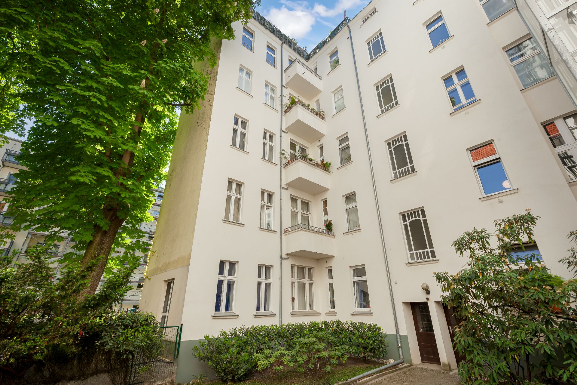 Innenhof eines Mehrfamilienhauses mit weißen Fassaden, Balkonen und Grünpflanzen.