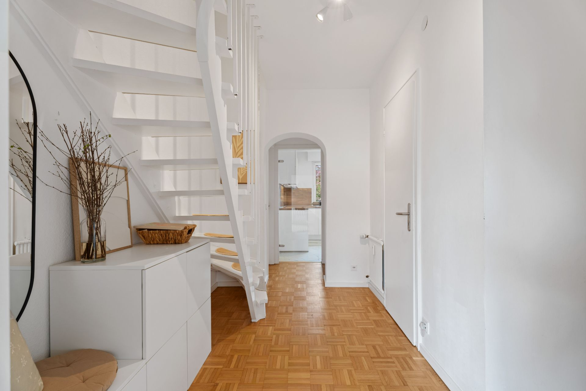 Heller Flur mit Holztreppe, Parkettboden und weißen Wänden in einem Wohnhaus.