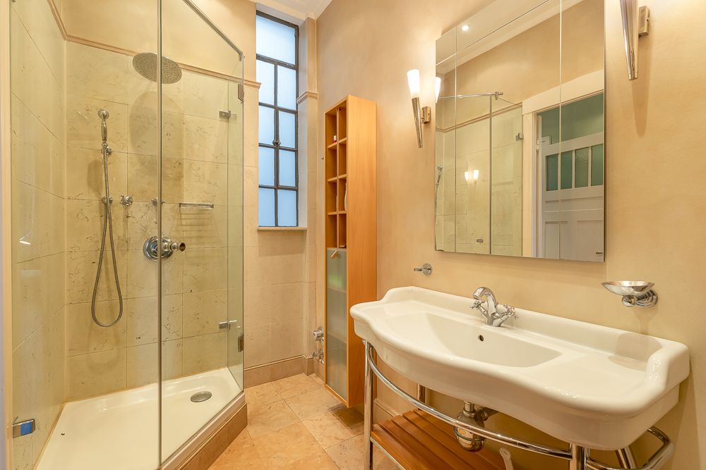 Modernes Badezimmer mit Glasdusche, großem Waschbecken und Spiegel, daneben ein Holzregal.