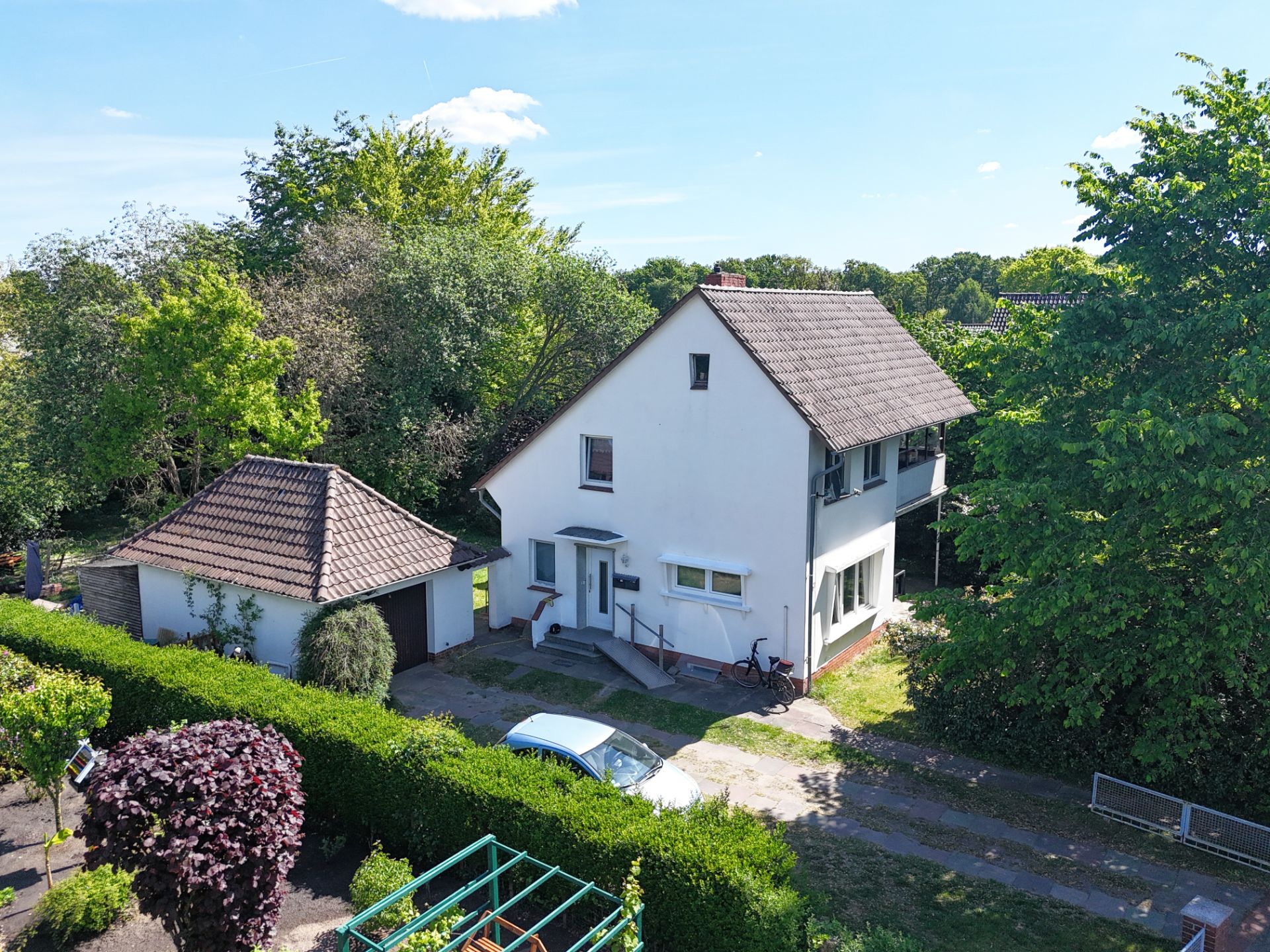 Weißes Einfamilienhaus mit Satteldach, Garage und Garten, umgeben von Bäumen.