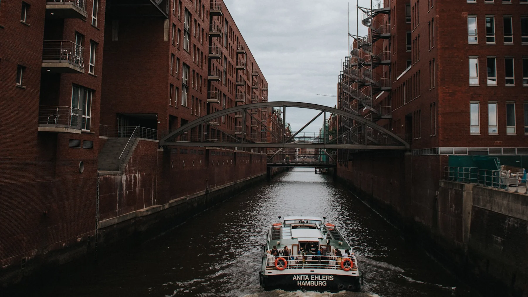 Boot fährt durch einen Kanal zwischen roten Backsteingebäuden mit Brücken darüber.