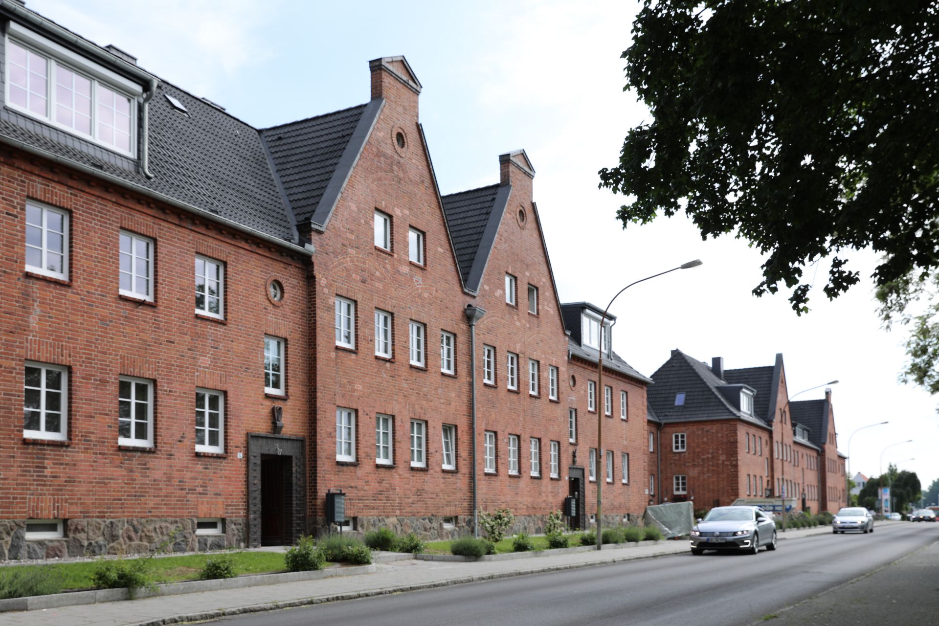 Reihenhaus aus rotem Backstein mit mehreren Fenstern an einer ruhigen Straße.