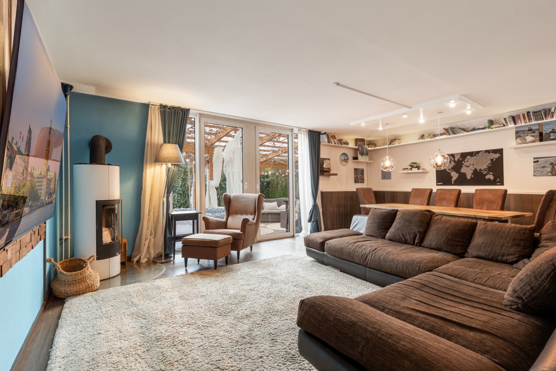 Modernes Wohnzimmer mit großer brauner Couch, Sessel, Kamin und Esstisch, Blick auf Terrasse.