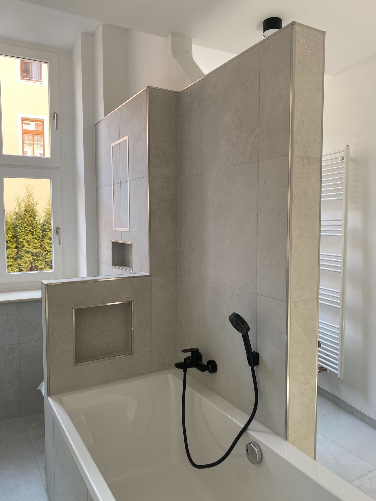 Modernes Badezimmer mit Badewanne, Duscharmatur, Nischen und Fenster.
