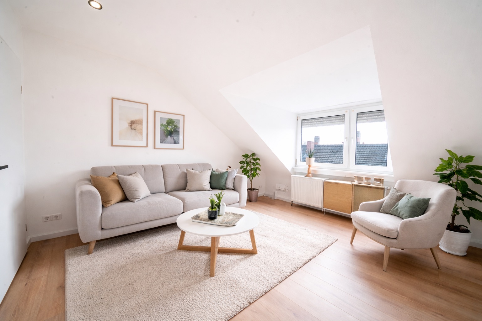 Helles Wohnzimmer mit Sofa, Sessel, Teppich, Couchtisch, Pflanzen und großen Fenstern.