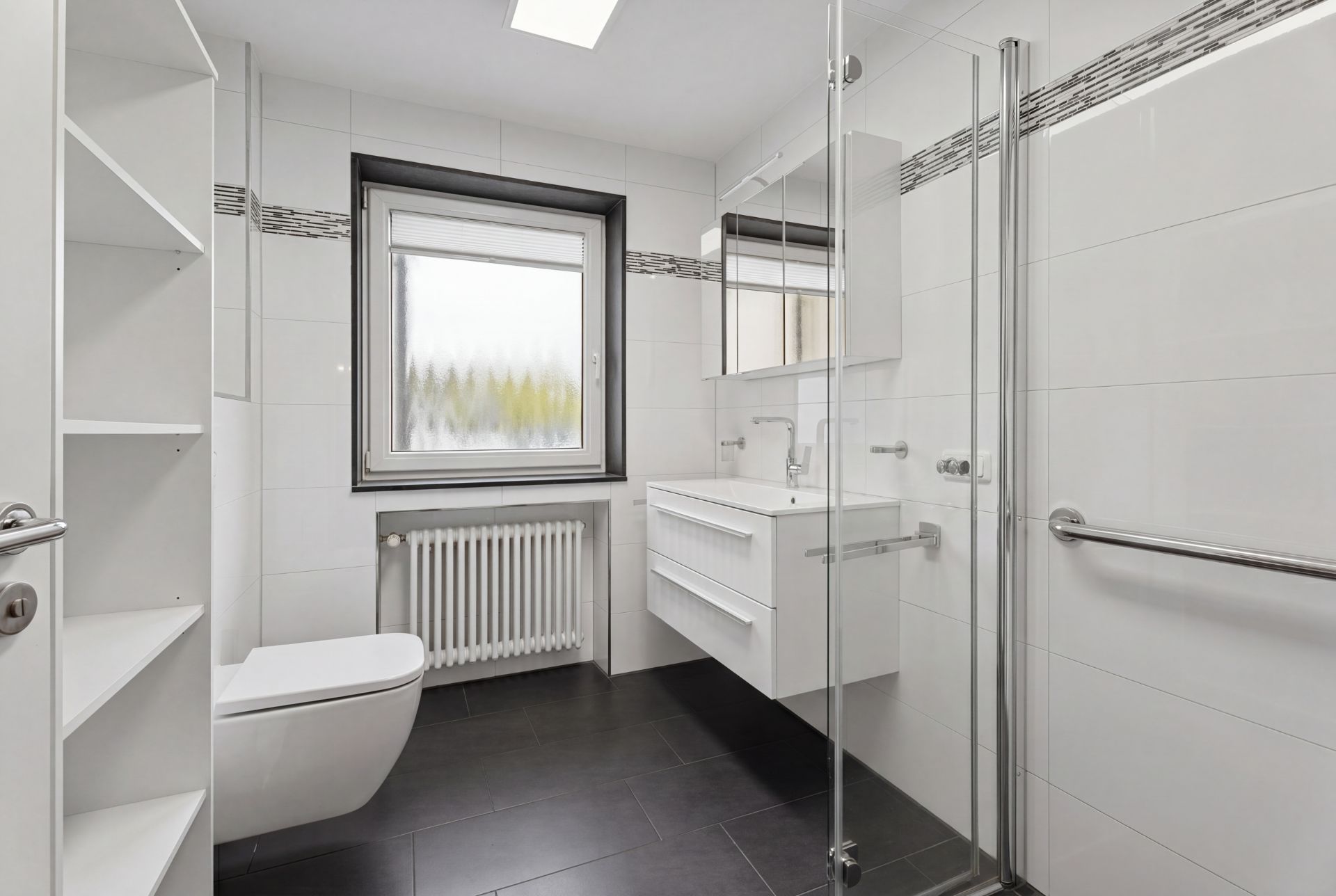 Modernes Badezimmer mit Dusche, WC, Waschbecken, Regalen und Fenster.