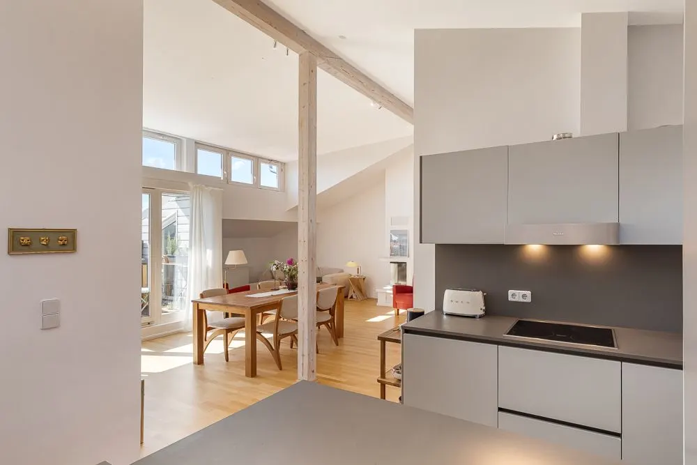 Moderne offene Küche mit grauen Schränken und Wohn- und Essbereich mit großen Fenstern.